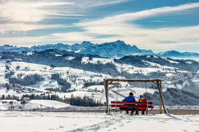 two people sitting on a bench in the snow at Dorfhus Gupf in Rehetobel