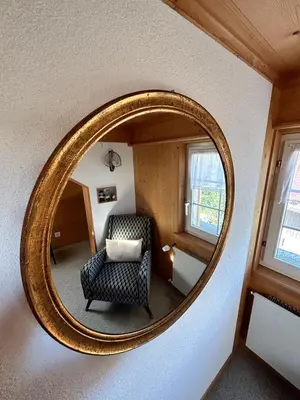 an oval mirror in a room with a chair at Wunderschöne Maisonette-Ferienwohnung in stattlichem Toggenburgerhaus in Sankt Peterzell