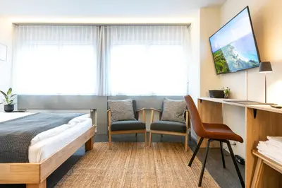 a hotel room with a bed and two chairs and a tv at INN JOY Apartments - Sankt Gallen Center in St. Gallen