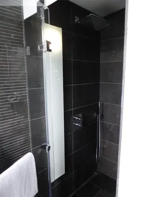 a bathroom with a shower with black tiles at Deluxe Zimmer in Privatwohnung an zentraler Lage in Teufen