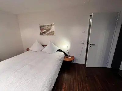 a bedroom with a bed with white sheets and a door at Deluxe Zimmer in Privatwohnung an zentraler Lage in Teufen
