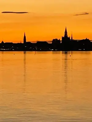 a sunset over the water with a city in the background at Ferienhäuschen mit privatem Seezugang in Bottighofen