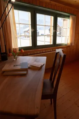a wooden table with a chair in a room with windows at Chammern in Nesslau