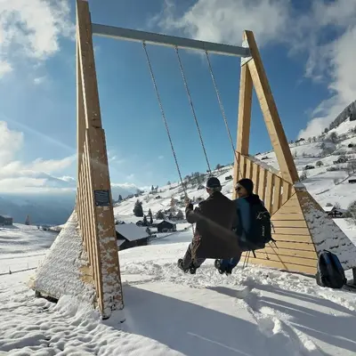 two people sitting on a swing in the snow at Ferienwohnung Halden in Unterwasser