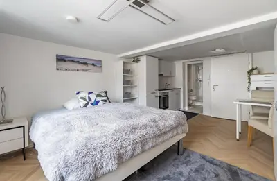 a white bedroom with a bed and a kitchen at Ferien Studio Wohnung Altstadt Multergasse 20 in St. Gallen