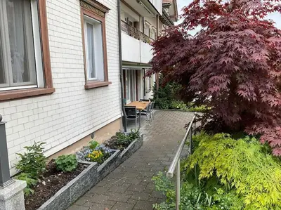 a patio of a house with a tree and some plants at 07 - Gästehaus Erika - Hundwil - Appenzellerland in Hundwil