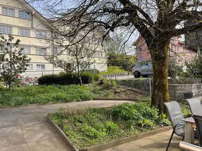 a tree and chairs in front of a building at 15 - Gästehaus Erika - Hundwil - Appenzellerland in Hundwil