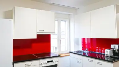 a kitchen with white cabinets and a red wall at Ninety Apartments in St. Gallen