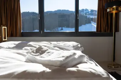 an unmade bed with white sheets in front of a window at Alpstern in Wildhaus
