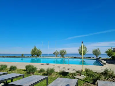 a swimming pool with picnic tables and the ocean in the background at Herberge Seeperle Bistro Rorschach in Rorschach