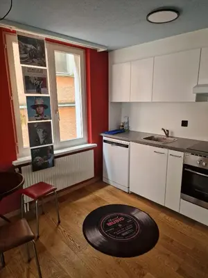 a kitchen with white cabinets and a red wall at Kugelgasse Apartments - Smart Living by Klang und Kleid in St. Gallen