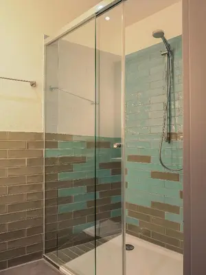 a glass shower in a bathroom with blue tiles at WYBA Living - Modernes Apartment - Gratis ÖV - Ruhig & Zentral in St. Gallen