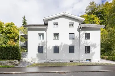 a white house with black windows on a street at Modernes Apartment mit Balkon und Parkplatz, Nähe See in St. Gallen
