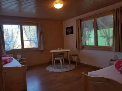 a bedroom with two beds and a table and two windows at Apartment Ferien im Gugger - Wohnung Stockberg by Interhome in Nesslau