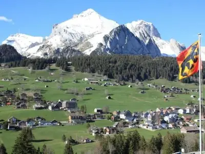 a flag flying in front of a village with snow capped mountains at Apartment Casa Uccello by Interhome in Wildhaus