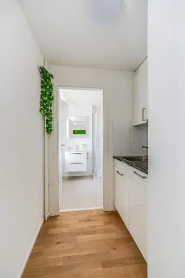 a kitchen with white cabinets and a wooden floor at Urban Hideaway Studio St Gallen Center in St. Gallen