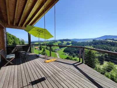 a wooden deck with a green umbrella and chairs on it at Ihre Wohlfühloase in Schwellbrunn