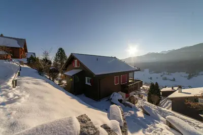 a house in the snow with the sun in the background at Studio Muerner in Wildhaus