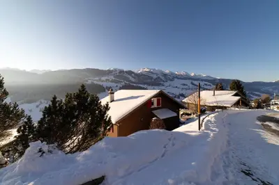 a house covered in snow with mountains in the background at Studio Muerner in Wildhaus
