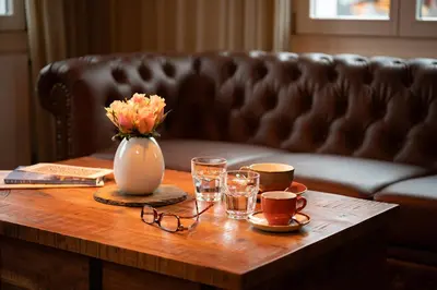 a coffee table with glasses and a vase of flowers and a couch at Hotel Garni Rössli in St. Gallen