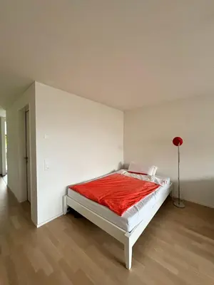 a white room with a bed with a red blanket at Neues Studio am Bodensee in Arbon