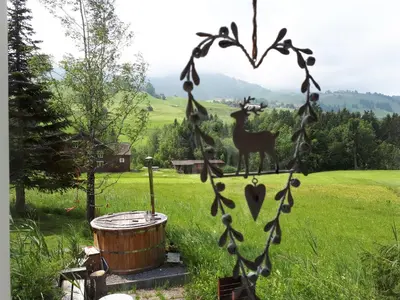 a hot tub in a field with a tree and mountains at Chalet Chic mit Hot Pot in Wildhaus
