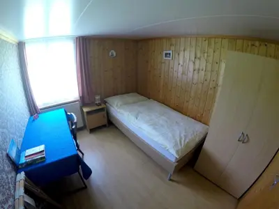 a small bedroom with a bed and a blue chair at Hotel Garni Traube B&B in Schwellbrunn
