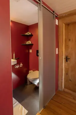 a bathroom with a toilet and a red wall at Gasthaus Rössli in Mogelsberg