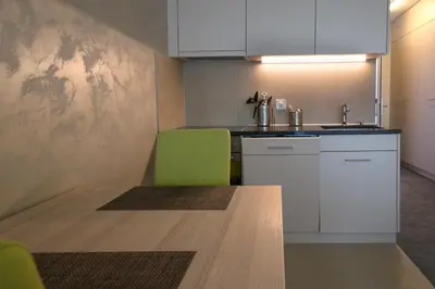 a kitchen with white cabinets and a green chair at wohnMOTEL - Hinterforst in Altstätten