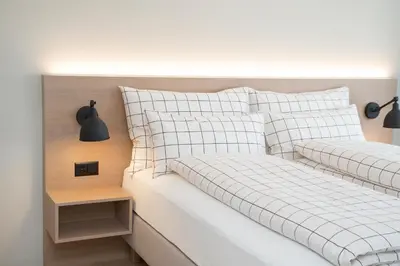 a bed with white sheets and pillows and a night stand at Businesshotel Forum Widnau in Widnau