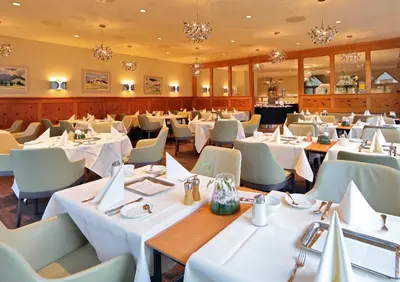 a dining room with tables and chairs and chandeliers at Hof Weissbad Health & Wellness Resort in Weissbad