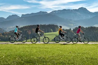 three people riding bikes on a road with mountains in the background at Bären - Das Gästehaus in Gais