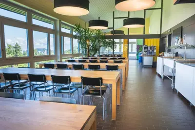a cafeteria with tables and chairs and windows at St. Gallen Youth Hostel in St. Gallen