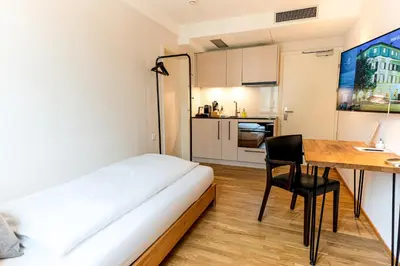 a small room with a bed and a desk and a kitchen at Hotel Le Lion - Self Check-in in Bischofszell