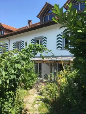 a white house with black shuttered windows and bushes at Bodensee Moosburg Biohof am See in Güttingen