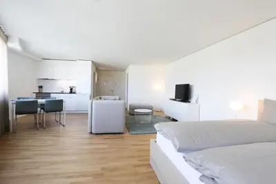 a white bedroom with a bed and a kitchen at Uze Apartments in Uzwil SG in Uzwil
