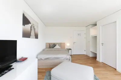 a white bedroom with a bed and a tv at Uze Apartments in Uzwil SG in Uzwil