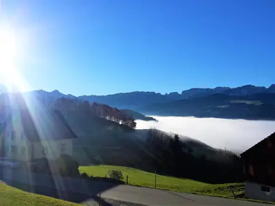a view of a foggy valley with a house and the sun shining at Gasthaus Bären Schlatt in Appenzell