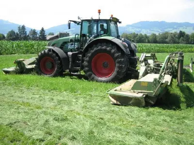 a green tractor sitting in a field with a mower at Steigmatt Bauernhof- Erlebnis in Montlingen