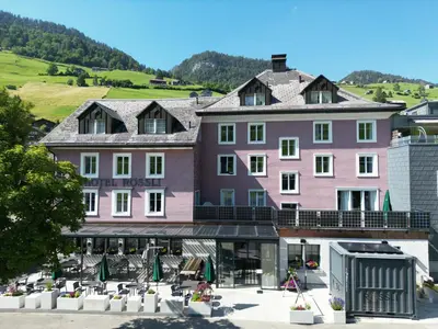 a large pink hotel with a hill in the background at Hotel Restaurant Rössli in Alt Sankt Johann