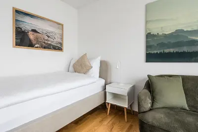 a white bedroom with a bed and a chair at SOHO F !Gratis Parken, Free Parking! in Kreuzlingen