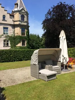 a wicker couch sitting in the grass in front of a house at Schloss Brunnegg in Kreuzlingen