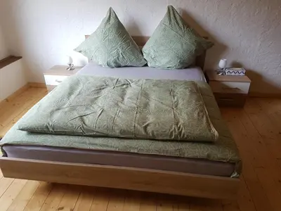 a bed with green sheets and pillows in a room at Bio Hof Moosburg am See mit Sauna in Güttingen
