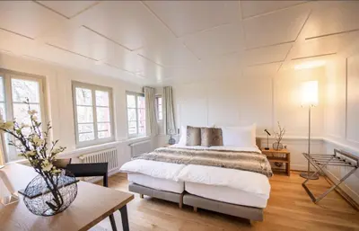 a white bedroom with a bed and a table at Hotel Restaurant Falkenburg in St. Gallen