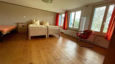 a bedroom with a bed and a chair and windows at Gästehaus am Sonnenfeld in Sommeri