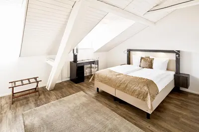 a white bedroom with a bed and a table at Hotel Schäfli in Uzwil