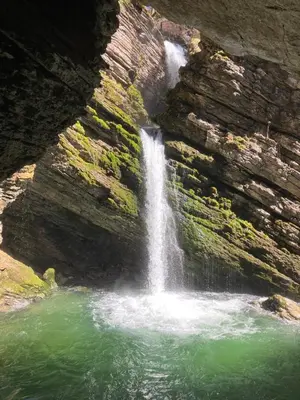 a waterfall on the side of a cliff with green water at Ferienwohnung Haus am Bach in Toggenburg in Wildhaus