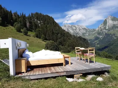 a bed and two chairs on a wooden deck with a mountain at Ferienwohnung Haus am Bach in Toggenburg in Wildhaus