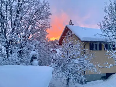 a house covered in snow with a sunset in the background at Ferienwohnung Haus am Bach in Toggenburg in Wildhaus