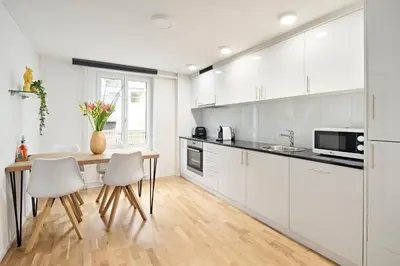 a kitchen with white cabinets and a wooden table and chairs at VISIMO Apartments Felsenstrasse St Gallen - Elegant heritage building in a quiet neighbourhood in St. Gallen